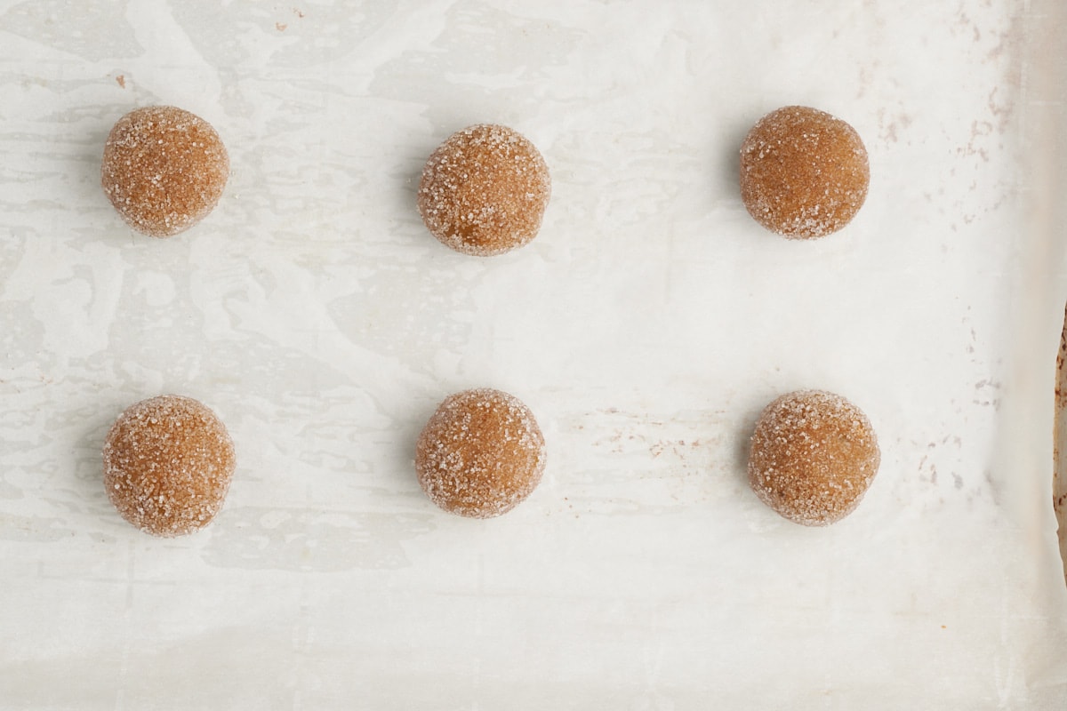 balls of ginger cookie dough on parchment lined baking sheet.