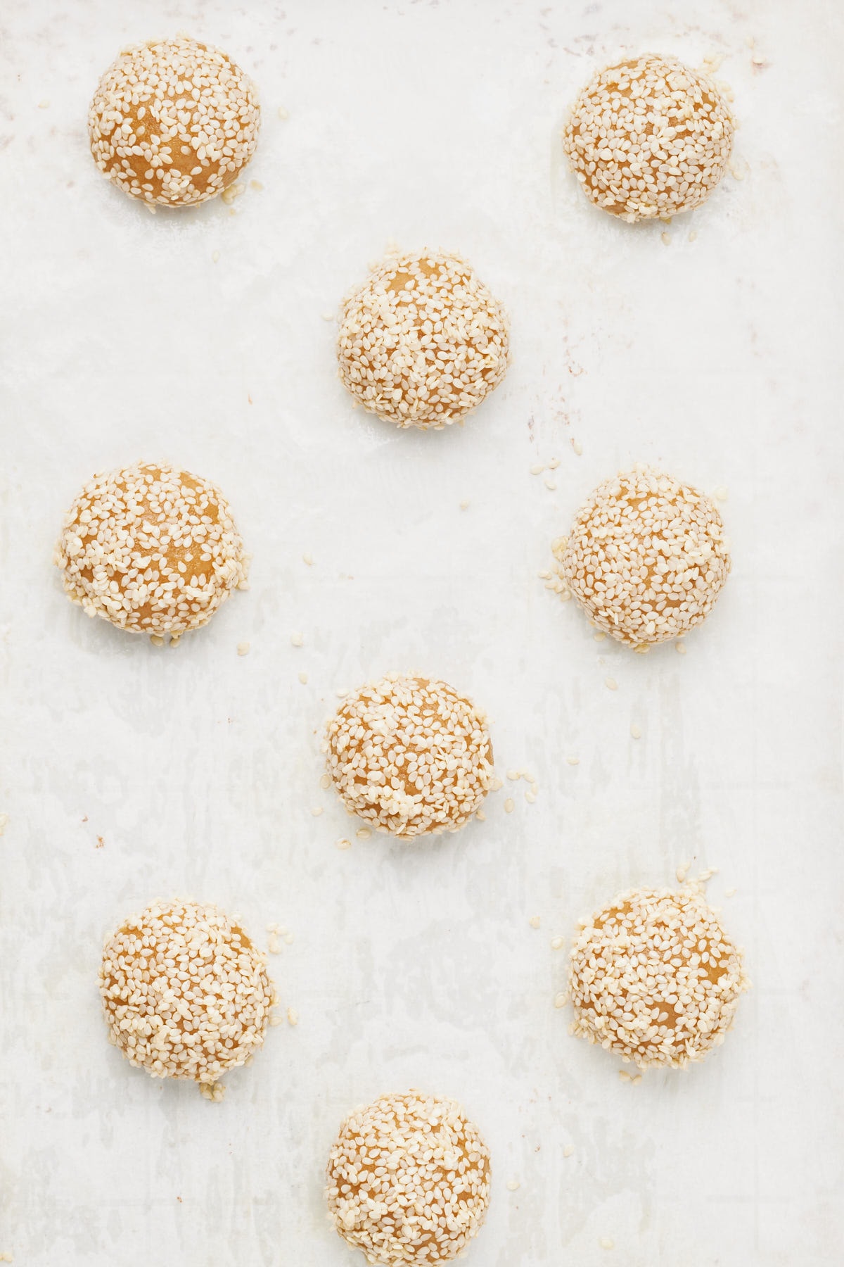 cookie dough balls coated with sesame seeds on a baking tray.